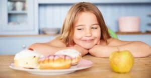 Girl Sitting At Table Choosing Cakes Or Apple For Snack